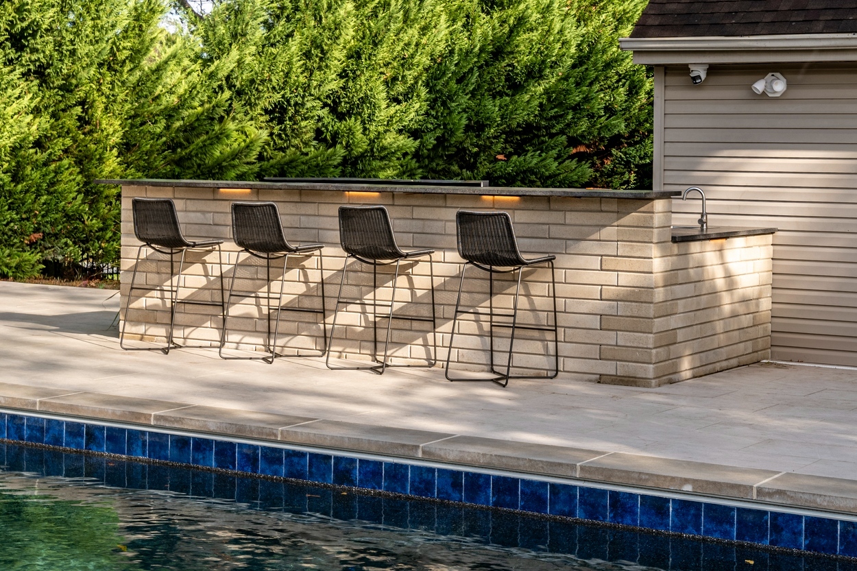 Outdoor bar area with four bar stools and neutral-toned custom hardscaping in Wilmington, DE