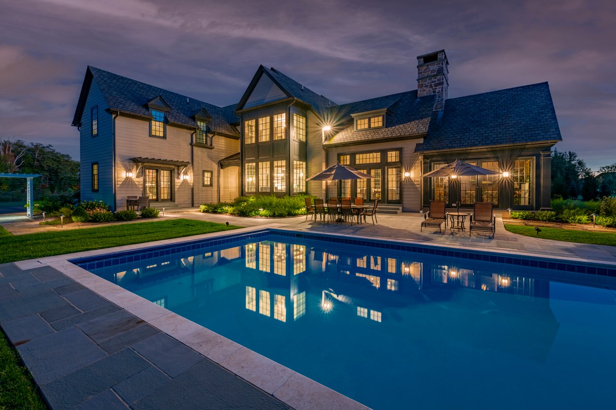 Nighttime poolside view with exterior lighting and hardscape accents highlighting custom hardscaping, landscaping and lighting in Wilmington, DE