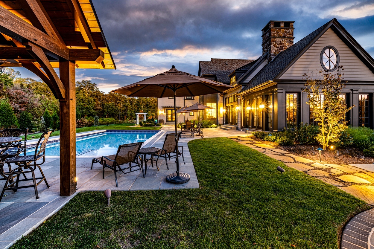 Twilight poolscape with umbrella seating and garden beds showcasing custom hardscaping, landscaping and lighting in Wilmington, DE