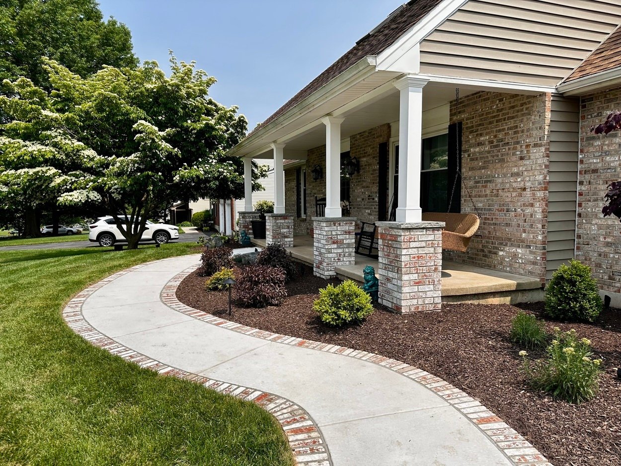 Curved concrete walkway with brick trim leading to a front porch in custom hardscaping and landscaping in Wilmington, DE