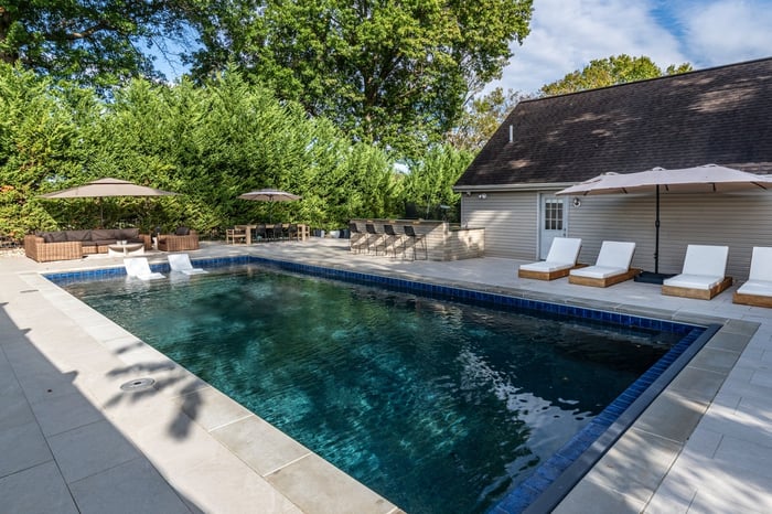 Custom pool featuring porcelain pavers, in-pool loungers, and pool house in Wilmington, DE