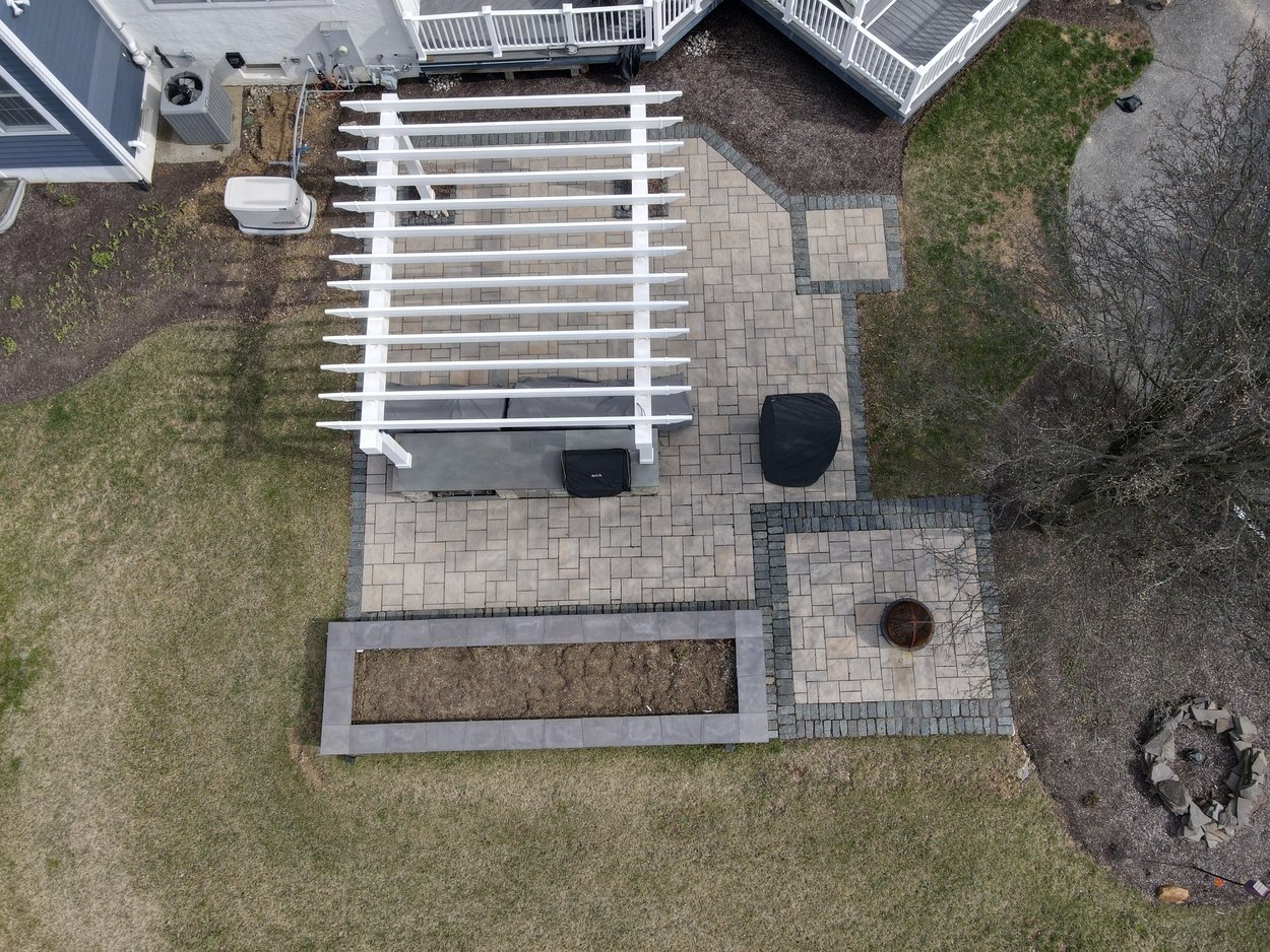 Aerial view of a pergola and paved patio with fire pit for an outdoor living project in Newark, DE