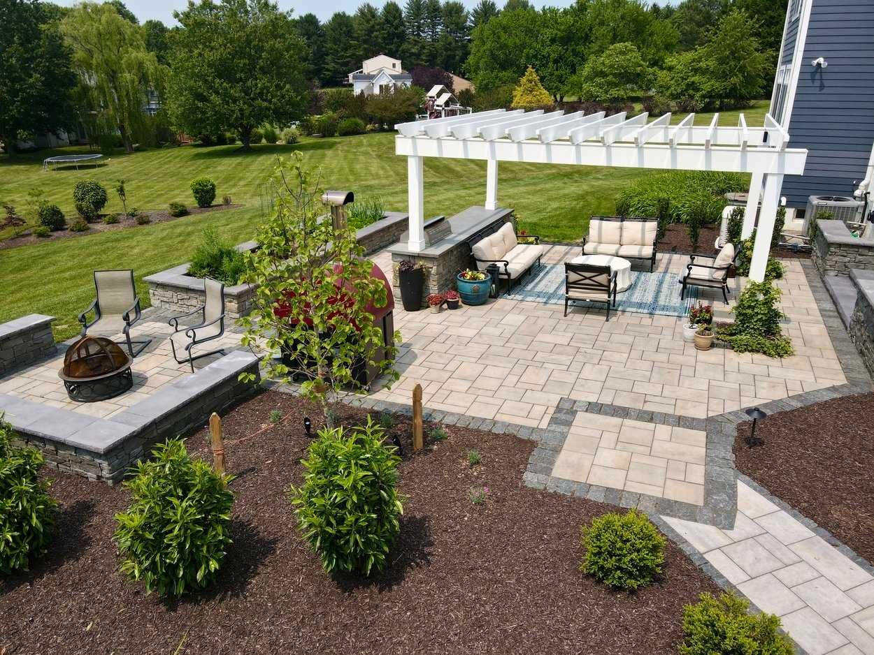 Paved patio with pergola and firepit among landscaping in an outdoor living project in Newark, DE
