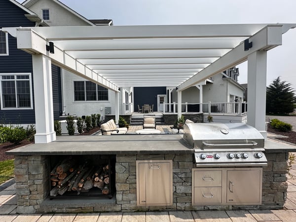 Stone kitchen island and built-in grill and wood storage with lounge area in an outdoor living project in Newark, DE