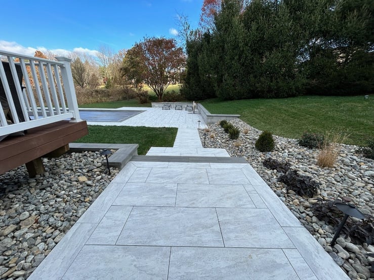 A scenic porcelain walkway leading from a raised deck to a stunning backyard pool in Newark, DE by First Class Lawn Care.
