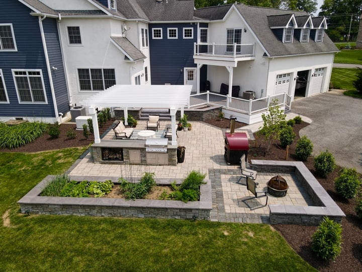 Newly hardscaped backyard featuring an outdoor kitchen, pergola, patio pavers, and firepit