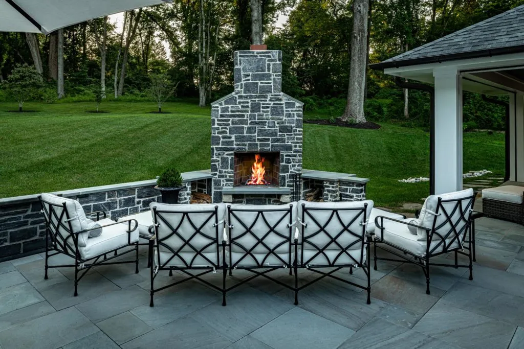 Masonry outdoor fireplace with black and white chairs around on patio
